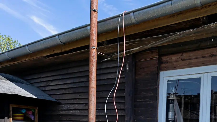 Kleine Solaranlage Zwei Kabelstränge hängen an einer rostigen Stange von einem Dach einer Holzhütte herunter.