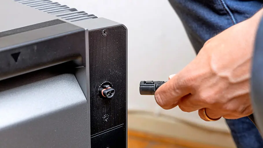 Kleine Solaranlage Eine Hand hält einen Stecker, der in einen Anschluss eines grauen Geräts gesteckt wird, daneben eine Person.