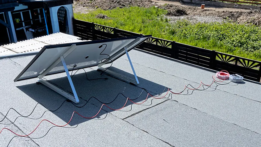 Kleine Solaranlage Ein Solarpanel ist auf einem Flachdach montiert, lange rote und schwarze Kabel führen über die Dachfläche.
