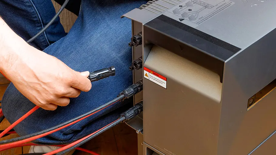 Kleine Solaranlage Ein Mann schließt mehrere rote und schwarze Solarkabel an die Rückseite einer Energiespeicherbox im Zimmer an.