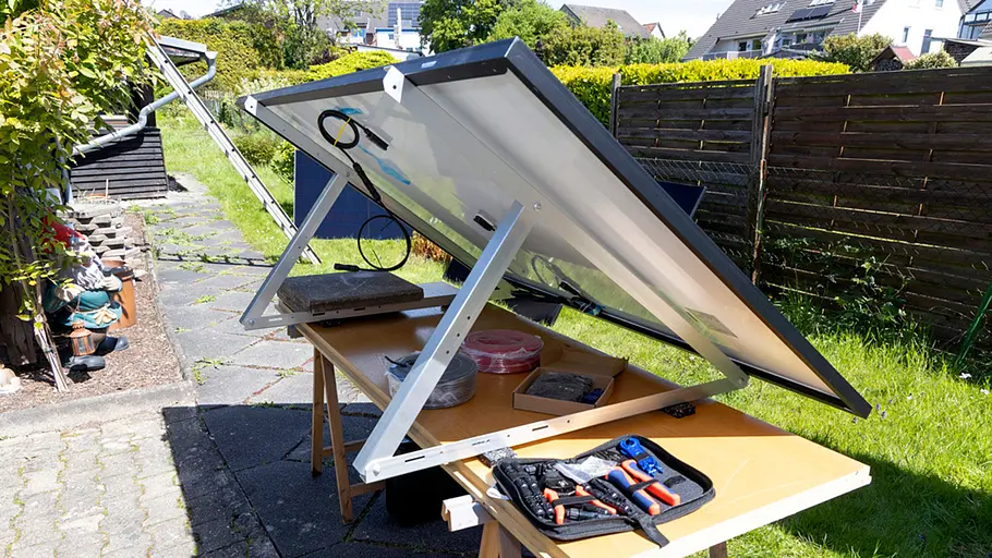 Kleine Solaranlage Ein Solarpanel ist schräg auf einem Gestell montiert, Werkzeug und Kabel liegen auf dem Tisch im sonnigen Garten.