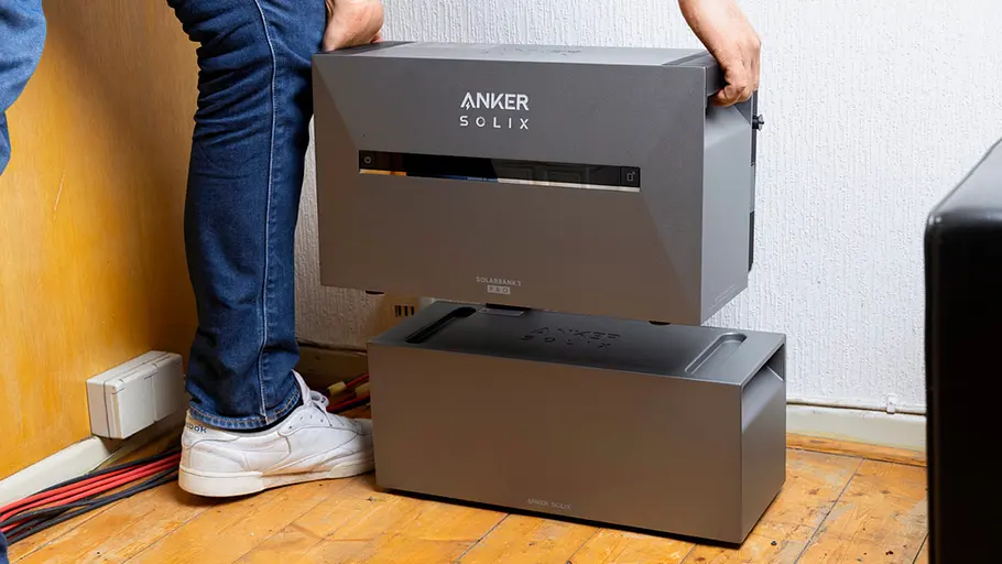 Kleine Solaranlage Eine Person stellt ein graues Modul mit der Aufschrift „Anker Solix“ auf ein weiteres gleiches Gerät im Zimmer.