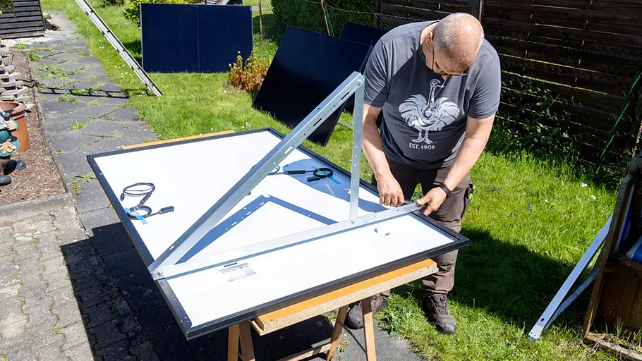 Kleine Solaranlage Ein Mann montiert im Garten ein Metallgestell an der Rückseite eines Solarpanels, Werkzeug liegt auf dem Tisch.