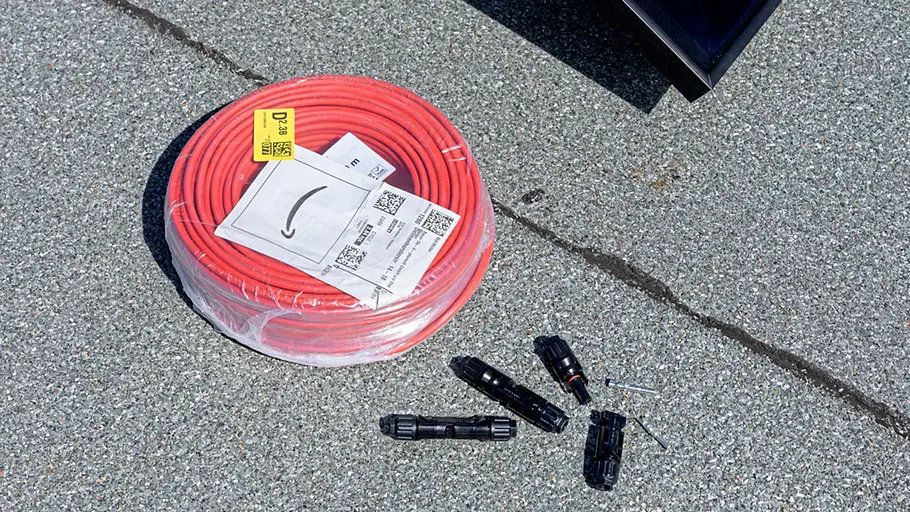 Kleine Solaranlage Eine Rolle rotes Solarkabel und mehrere schwarze Stecker liegen auf einem Flachdach neben einem Solarpanel.