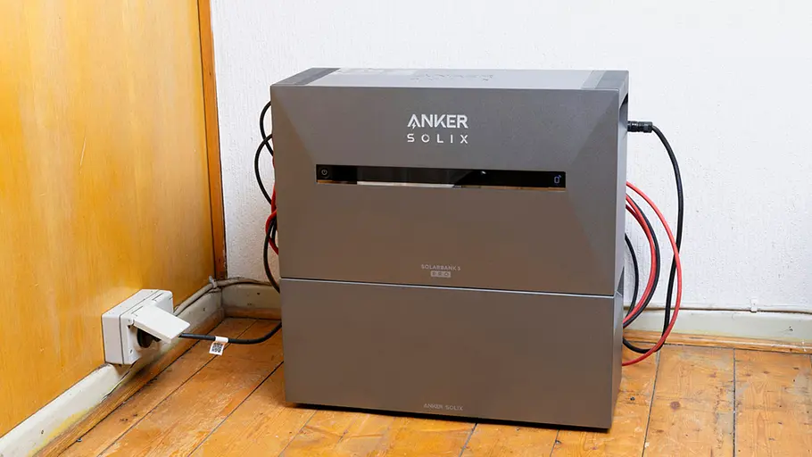 Kleine Solaranlage Ein grauer Energiespeicher mit der Aufschrift „Anker Solix“ steht mit angeschlossenen Kabeln neben einer Wandsteckdose.