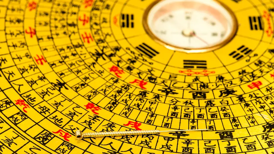 Chinesischer Feng-Shui-Kompass Detailaufnahme eines chinesischer Feng-Shui-Kompasses: rund um die Kompassnadel sind rote und schwarze chinesische Schriftzeichen auf gelben Grund zu sehen.