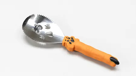 Ein Kürbisschaber zum Schnitzen von Kürbissen. Die Griffe sind wie orangene Finger mit schwarzen Nägeln geformt.