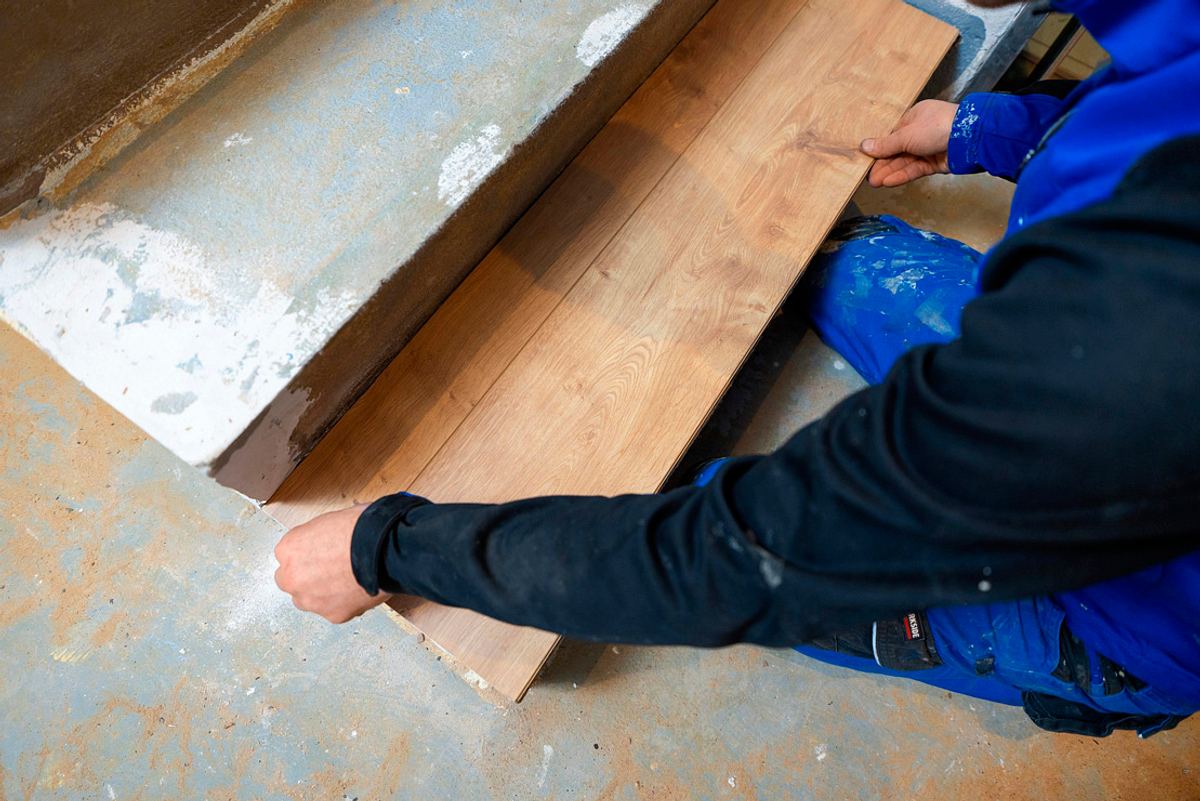 Laminatdiele wird mit beiden Händen auf die vorbereitete Stufe gelegt und angedrückt