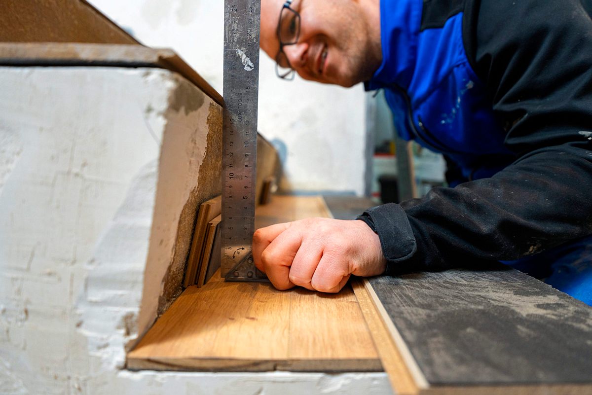 Handwerker richtet ein Laminatstück mit großem Winkel an der Treppenwange aus.