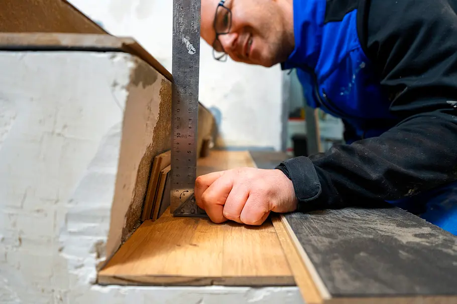 Handwerker richtet ein Laminatstück mit großem Winkel an der Treppenwange aus.