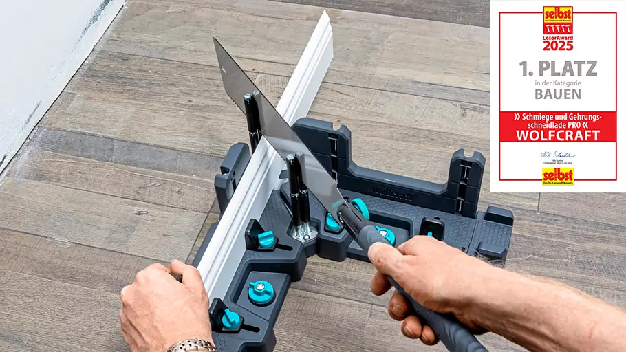 Leseraward Gewinner Bauen Zwei Hände schneiden eine weiße Leiste mit einer Gehrungssäge und einer Schneidlade auf einem Holzboden zurecht.