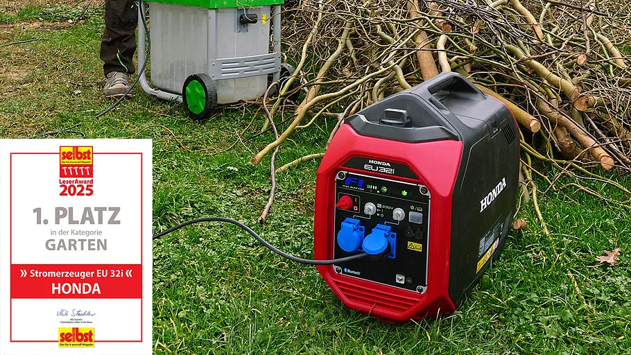 Leseraward Gewinner Garten Ein rotes Honda Stromaggregat steht auf einer Wiese vor Ästen, daneben ein Gartenhäcksler mit grünem Deckel.