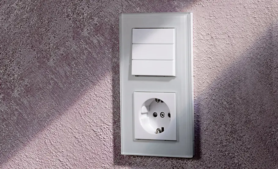Lichtschalter wechseln Ein fertiger Lichtschalter und eine Steckdose sind nebeneinander an einer hellen Wand montiert.