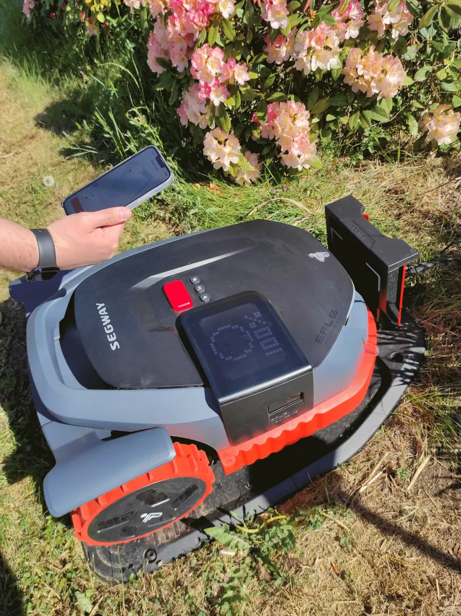 Im Test erkannte die App den Mähroboter bereits nach wenigen Sekunden. Mähroboter der Marke Segway befindet sich in seiner Ladestation. Über ihm ist eine Hand mit Smartphone zu sehen.
