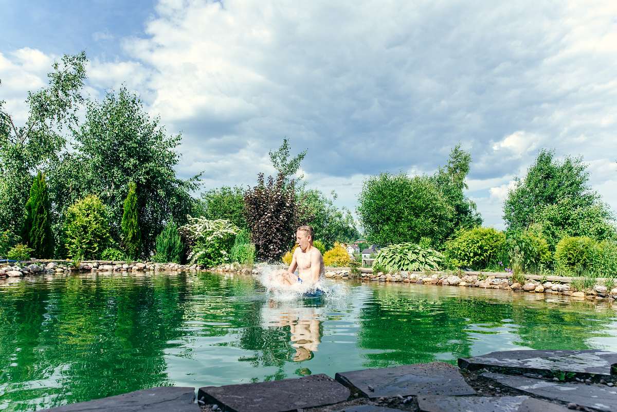 Schwimmteich In Junge springt in den Schwimmteich, das Wasser spritzt hoch über den Rand.