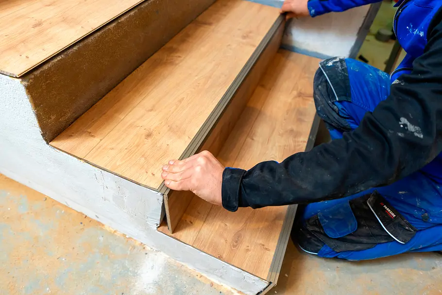 Ein Mann justiert die neu angebrachte Holzstufe auf einer Betontreppe.