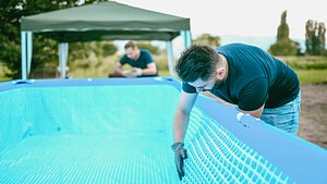 Man greift in gefüllten Pool, um die undichte Stelle zu lokalisieren - Foto: Pool flicken