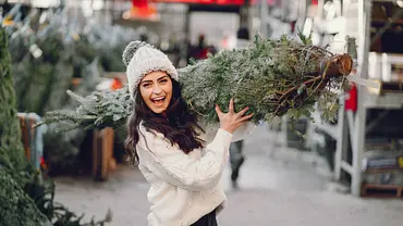 Eine junge Frau in weißem Wollpulli und Pudelmütze hat einen Tannenbaum geschultert und trägt ihren Einkauf glücklich nach Hause! - Foto: iStock / VNWB Eine junge Frau in weißem Wollpulli und Pudelmütze hat einen Tannenbaum geschultert und trägt ihren Einkauf glücklich nach Hause! - Foto: iStock / VNWB