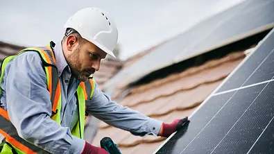 Ein Bauarbeiter schraubt ein Solarpanel auf ein schräges Hausdach - Foto: istockphoto.com / Drazen Zigic