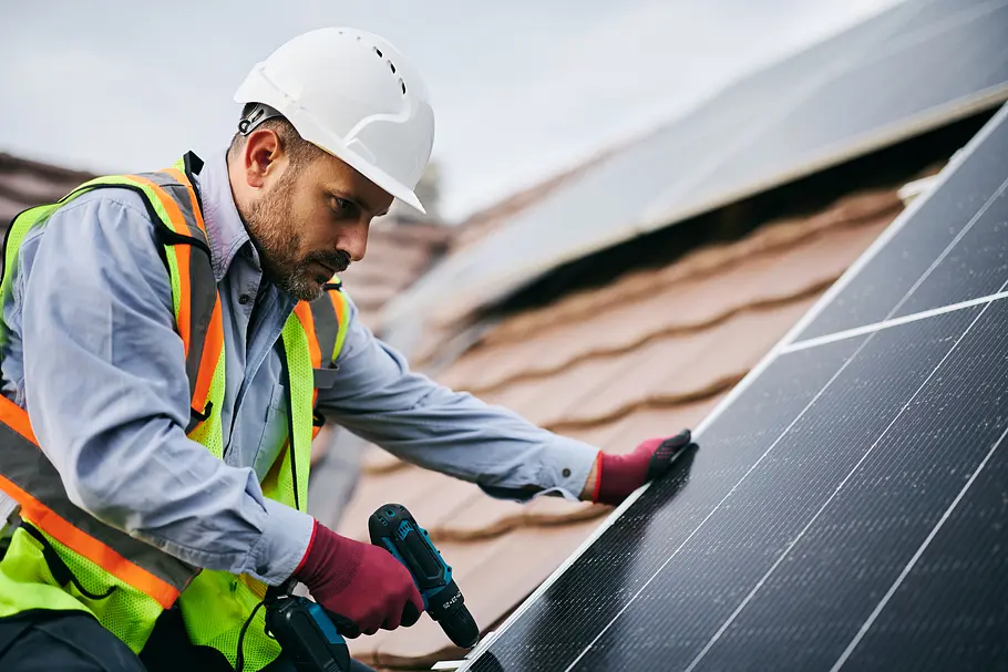 pv-anlage-planung-aufbau Ein Bauarbeiter schraubt ein Solarpanel auf ein schräges Hausdach