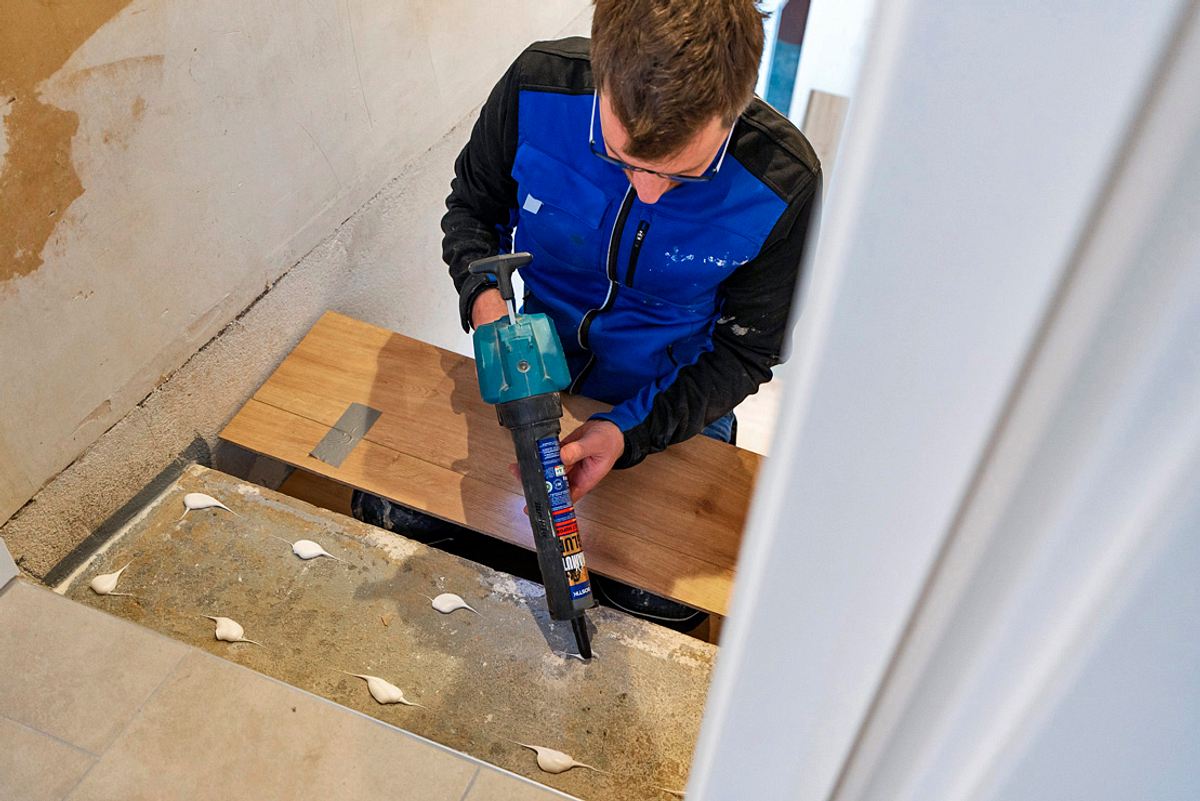 Handwerker trägt Montagekleber auf eine untere Treppenstufe auf, Ansicht von oben.