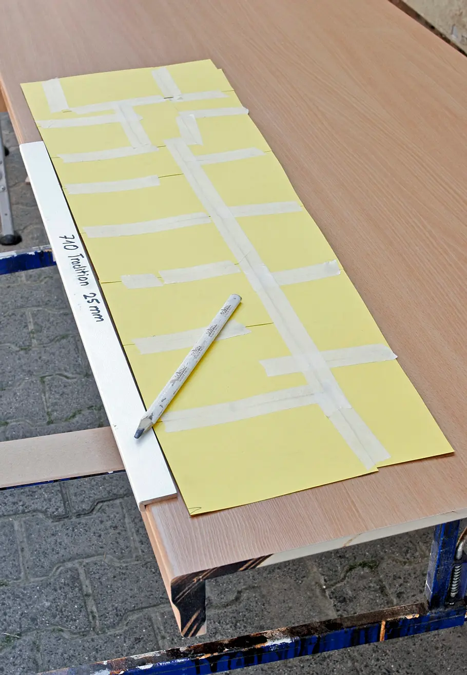 Eine gelbe Schablone wird auf eine Holzplatte gelegt, daneben liegt ein Stift.