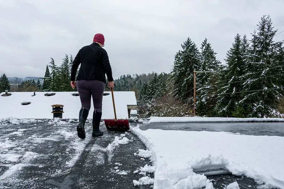 Ein Mann entfernt mit einer Schneeeschaufel Schnee von einem Flachdach