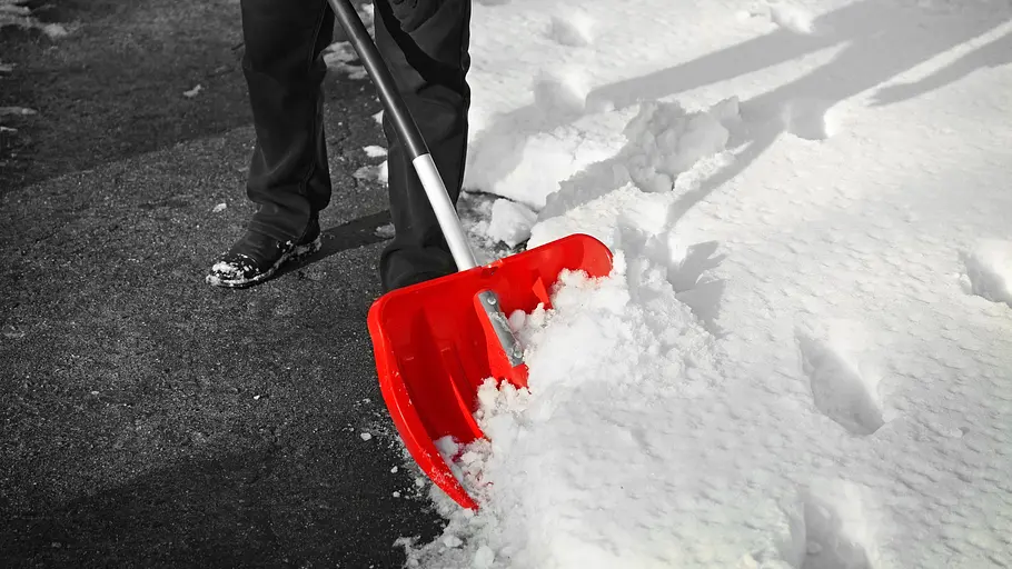 Schnee räumen Eine Person schippt mit einer knallroten Schneeschaufel Schnee.