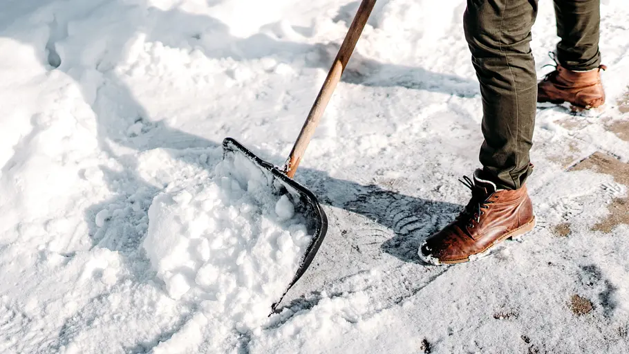 Schnee räumen Ein Mann in braunen Winterstiefeln befreit den Gehweg mit einer schwarzen Schneeschaufel von Schnee.