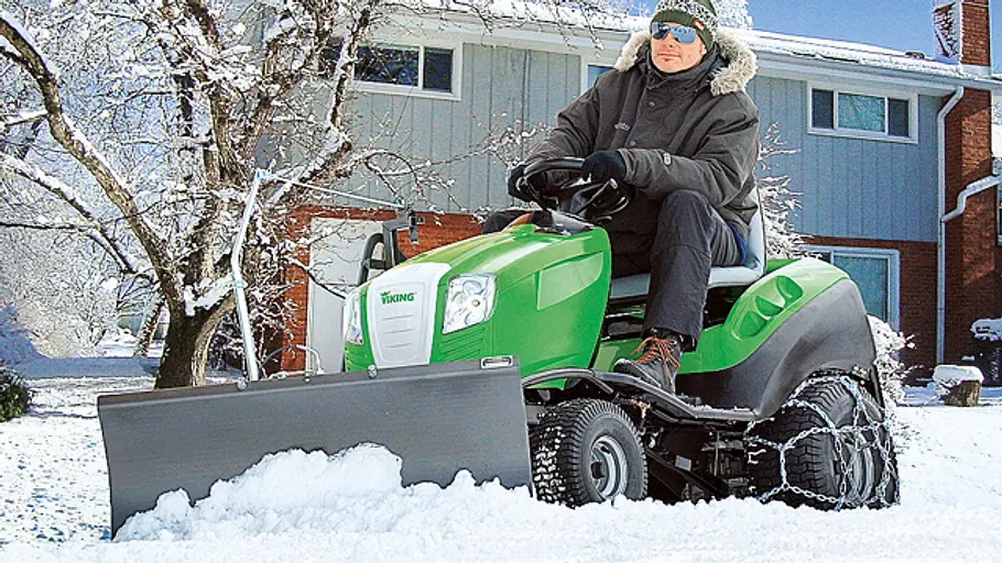 Rasentraktor mit Schneeräumschild Mann fährt auf seinem grünen Rasentraktor mit Schneeräumschild durch dichten Schnee