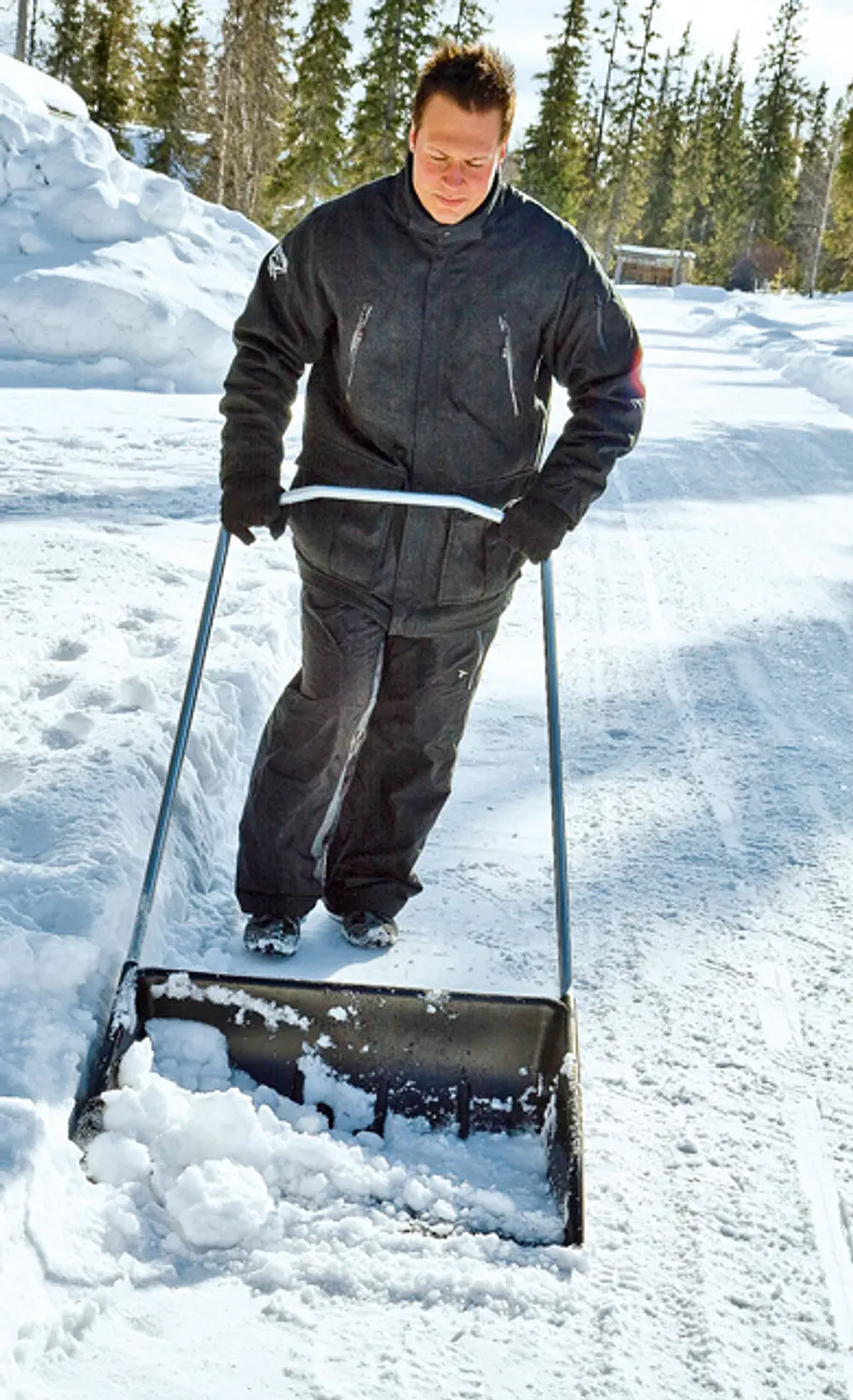 Schneewanne Ein Mann schiebt eine großformatige schwarze Schneewanne am Rand einer Schneewehe entlang.
