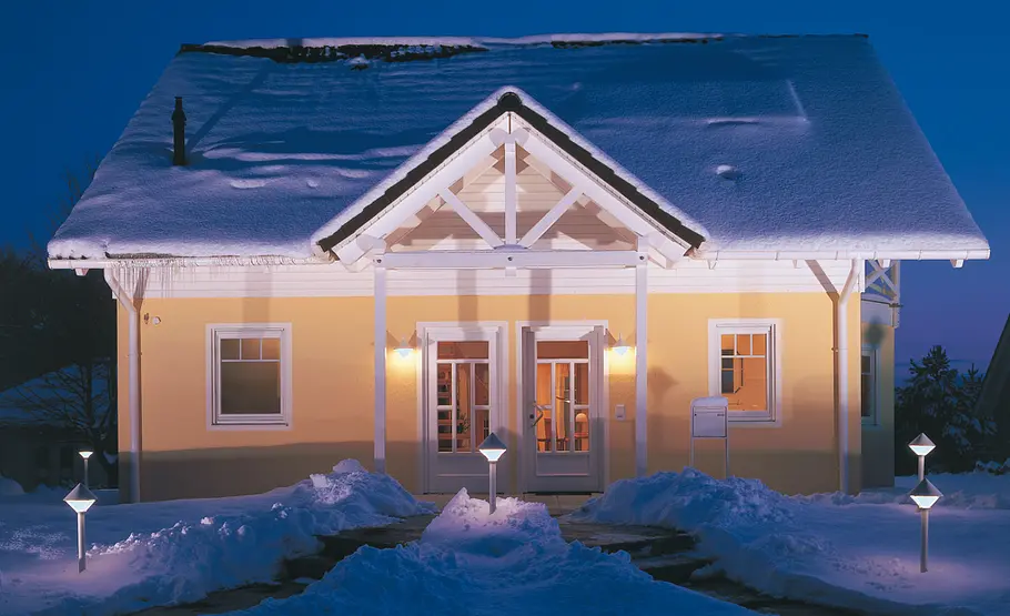 An einem freistehenden Einfamilienhaus hat sich Schnee auf dem Dach gesammelt und hängen spitze Eiszapfen an den Dachrinnen.