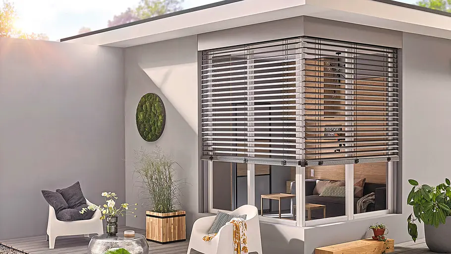 Smarte Beschattung: Jalousien Moderne Terrasse mit gemütlichen Sitzmöbeln, Pflanzen und großen Fenstern mit halb geschlossenen Lamellenjalousien.