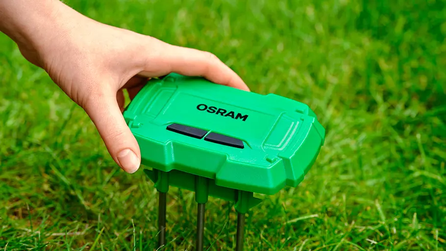 Bodenfeuchtesensor von Osram Eine Hand steckt einen grünen Osram Bodenfeuchtesensor mit Metallfüßen in eine Wiese.