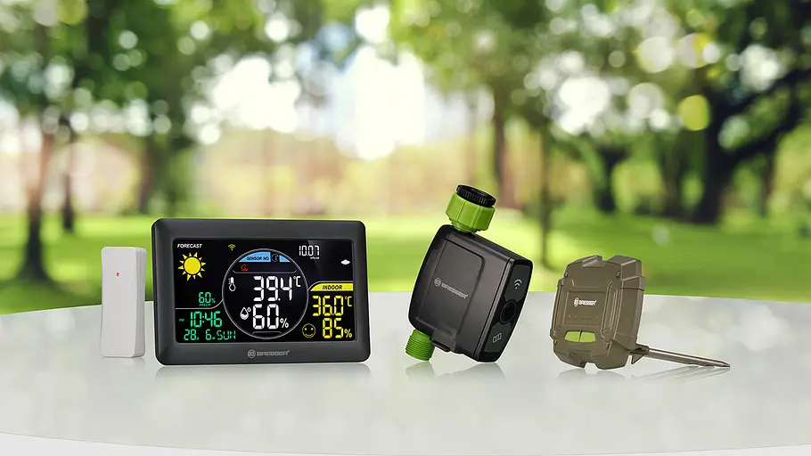 Bewässerungssystem von Bresser Ein digitales Display, ein Bewässerungsventil und ein brauner Bodensensor von Bresser stehen auf einem weißen Tisch im Garten.