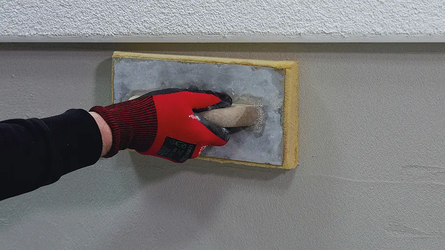 Sockel verputzen Eine Hand mit rotem Handschuh reibt mit einem Schwammbrett die noch feuchte Putzoberfläche an einer Wandfläche ab.