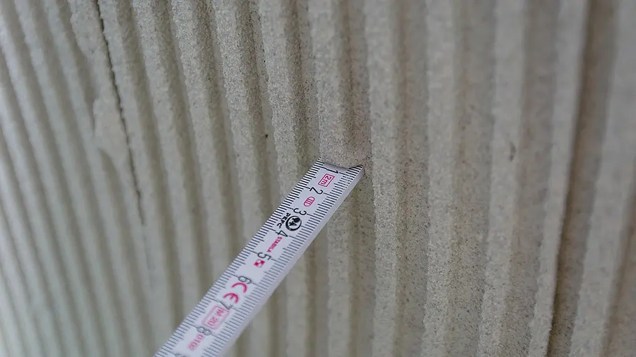 Sockel verputzen Ein Gliedermaßstab misst die Tiefe der Rillen in frisch aufgetragenem, strukturiertem Putz an einer Wand.