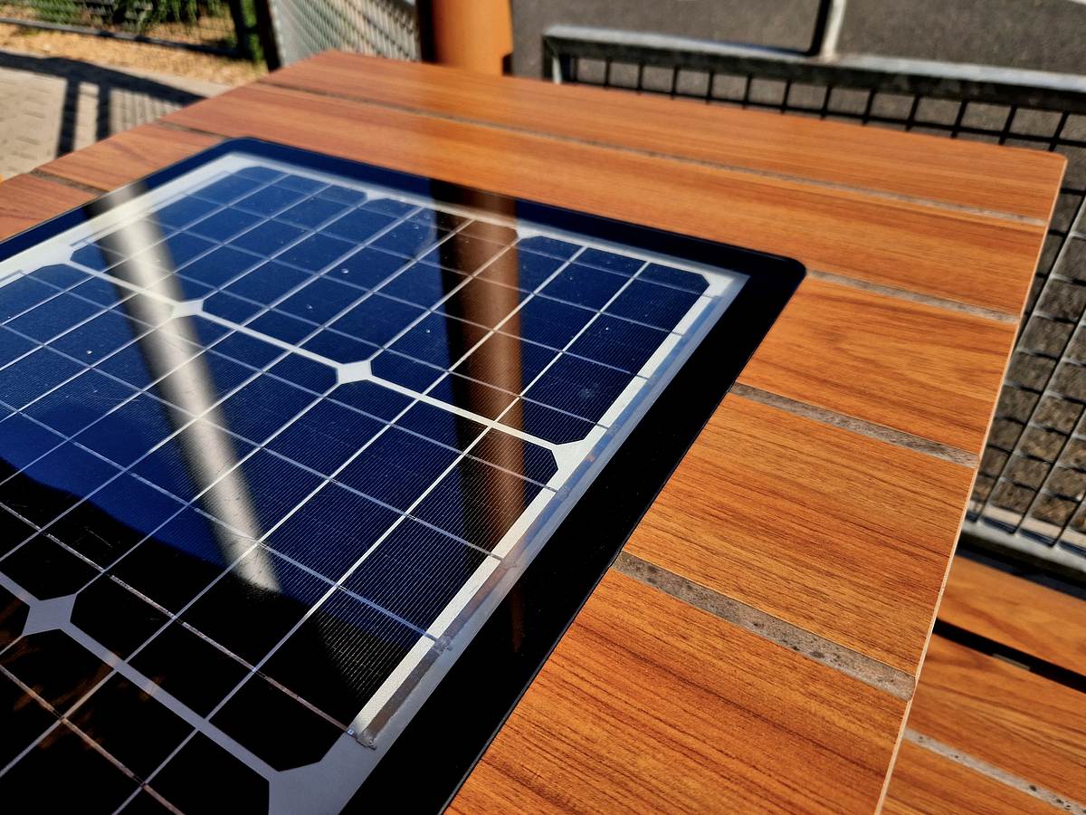 Eine Solarzelle ist in einen braunen Holztisch integriert. Die Solarzelle reflektiert blaues Licht im Sonnenschein.