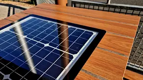 Eine Solarzelle ist in einen braunen Holztisch integriert. Die Solarzelle reflektiert blaues Licht im Sonnenschein. - Foto: istockphoto.com / beekeepx Eine Solarzelle ist in einen braunen Holztisch integriert. Die Solarzelle reflektiert blaues Licht im Sonnenschein. - Foto: istockphoto.com / beekeepx