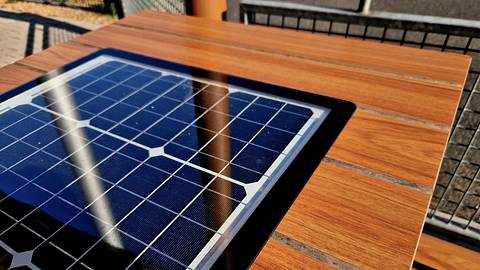 Eine Solarzelle ist in einen braunen Holztisch integriert. Die Solarzelle reflektiert blaues Licht im Sonnenschein. - Foto: istockphoto.com / beekeepx