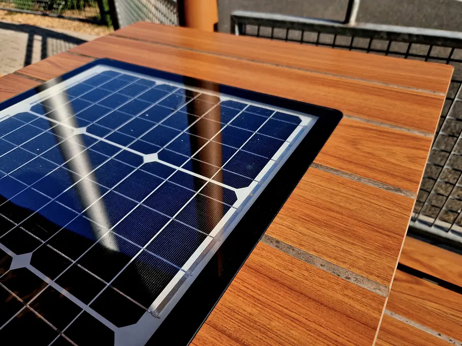 Eine Solarzelle ist in einen braunen Holztisch integriert. Die Solarzelle reflektiert blaues Licht im Sonnenschein.