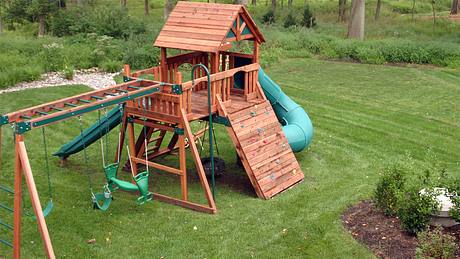Spielhaus mit Rutsche und Schaukel aus Holz steht in einem Garten - Foto: iStock/imagewerks