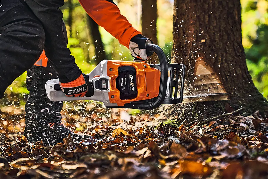 Person in Schutzkleidung beim Sägen eines Baumstamms mit einer STIHL Akku-Motorsäge im Wald.