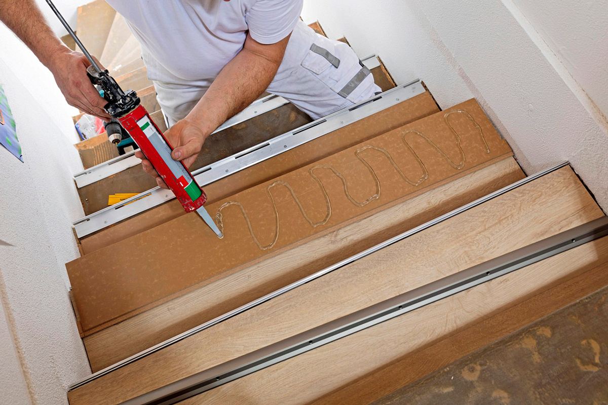 Mit einer Kartuschenpistole wird Kleber wellenförmig auf eine Treppenstufe aufgetragen.