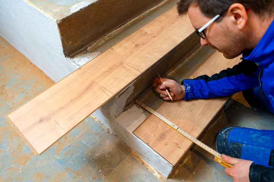 Handwerker misst mit Zollstock und Stift eine Laminatdiele auf der Treppe.