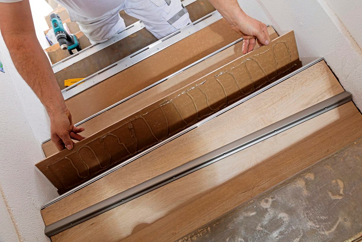 Ein Handwerker legt eine mit Kleber versehene Stufe in die Treppe ein.