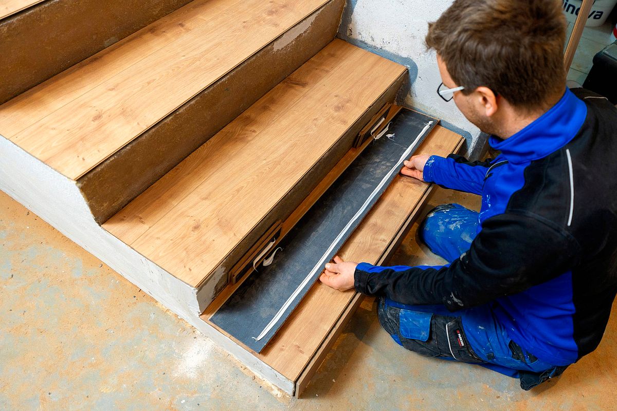Handwerker platziert Trittschalldämmung und Laminatteile an mehreren Treppenstufen.