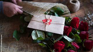 Zu einem Strauß roter Rosen passt eine Karte mit lieben Valentinstag-Sprüchen. - Foto: iStock / ArtistGNDphotography
