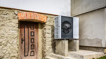 Wärmepumpe neben dem Eingang eines erkennbar alten Hauses mit Steinmauern und alter Holztür. - Foto: istockphoto.com / brebca Wärmepumpe neben dem Eingang eines erkennbar alten Hauses mit Steinmauern und alter Holztür. - Foto: istockphoto.com / brebca