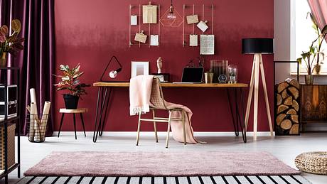 Ein Schreibtisch vor einer bordeauxfarbenen Wand mit rosa Accessoires - Foto: iStock / KatarzynaBialasiewicz